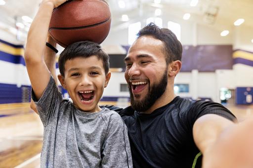 AAA Life -  Smiling father and son playing basketball in a gym. 